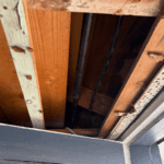 Black iron gas pipe with a vertical offset rising into wooden floor joists to feed an appliance on the floor above.