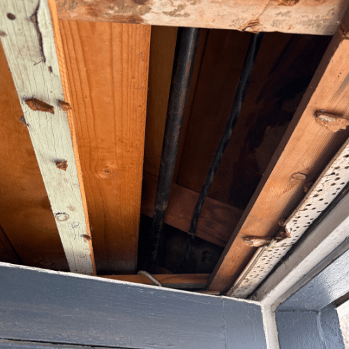 Black iron gas pipe with a vertical offset rising into wooden floor joists to feed an appliance on the floor above.