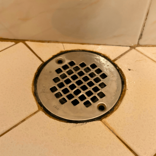 Professional plumber using drain auger tool to clear a shower drain clog in West Valley City.