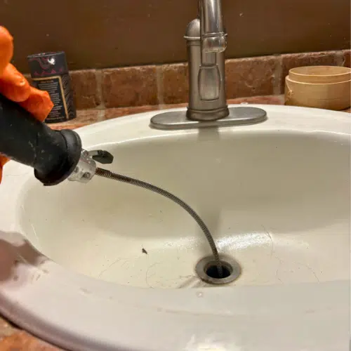 Inspecting the sink drain wall arm and venting connection during a West Jordan plumbing repair.