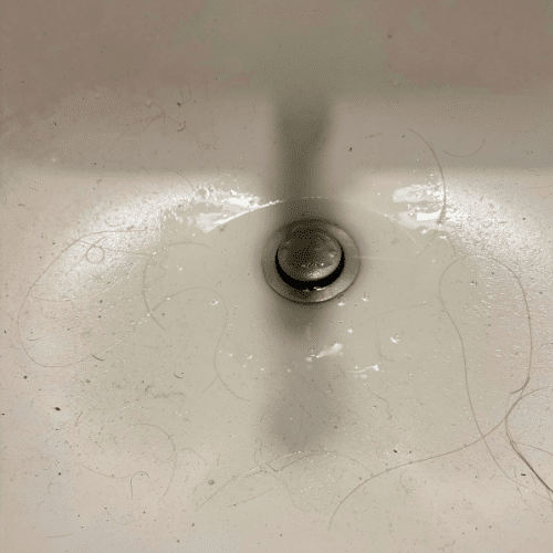 Inspecting the sink drain wall arm and venting connection during a West Jordan plumbing repair.