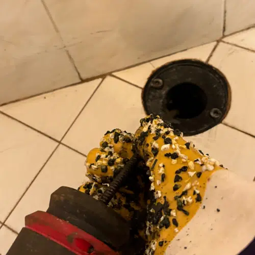 Professional plumber using drain auger tool to clear a shower drain clog in West Valley City.