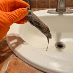 Inspecting the sink drain wall arm and venting connection during a West Jordan plumbing repair.