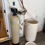 Old wall-mounted softener tank and open brine drum before removal during Millcreek water softener replacement job.