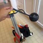 Hand holding the removed ball-cock style toilet fill valve next to the new Fluidmaster box after replacement in Salt Lake City.