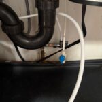 Blue-handled ice maker shutoff valve and tubing under sink near disposal drain in Salt Lake City kitchen