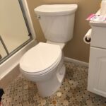 White customer-supplied tank toilet set on pebble tile after flange repair and shimming in West Jordan bathroom