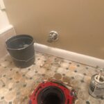 Reinforced red closet flange on tile floor with new chrome quarter-turn shutoff on the wall in West Jordan bathroom