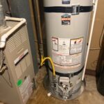 Lower Bradford White water heater base on pan with yellow gas flex, control, and seismic straps in Bountiful utility room