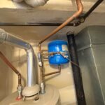 Copper piping, draft hood area, and blue expansion tank above the water heater top in a Salt Lake City condo mechanical room.