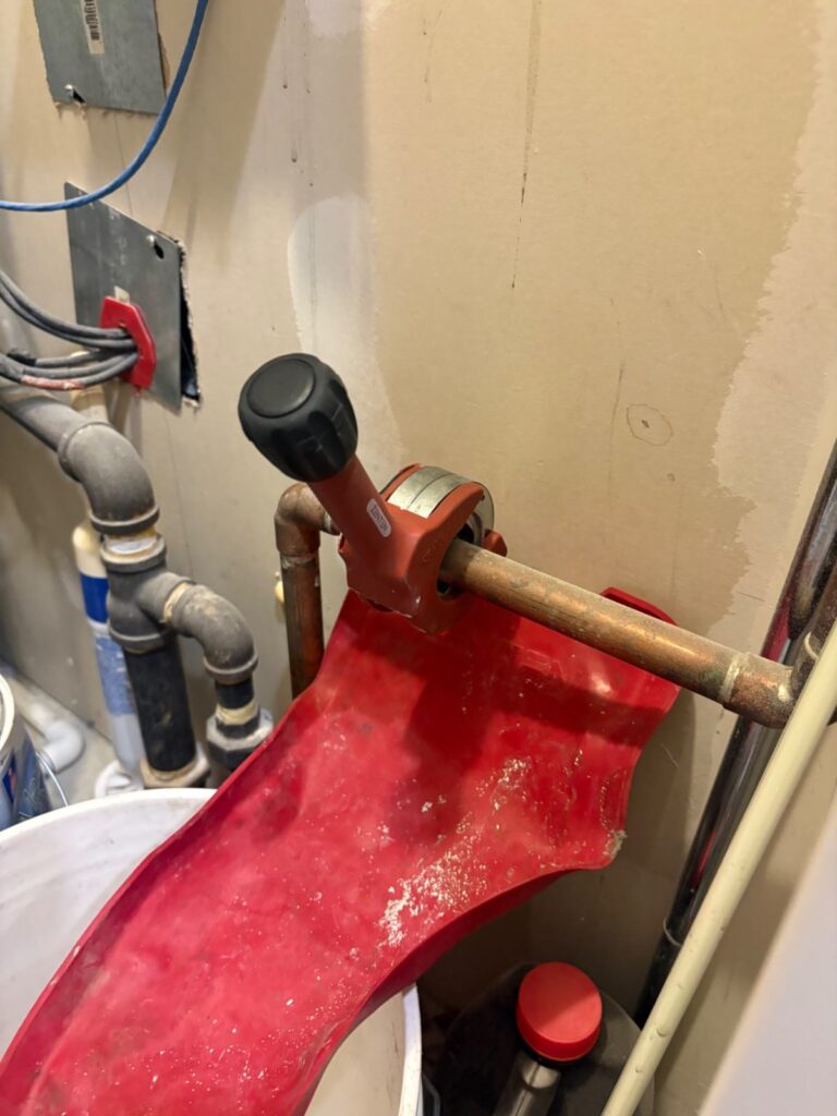 Ridgid pipe cutter on copper tubing over red drip tray in mechanical closet during install