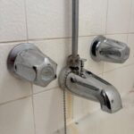 Chrome diverter tub spout with outside shower riser and dual handles on tiled wall before repair in Salt Lake City bathroom