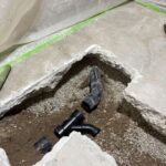 Black ABS fittings laid in open dirt and gravel under broken slab for new drain routing in Draper.