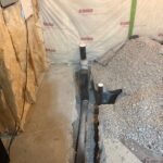Long black drain run and upright stubs in gravel trench after laundry kitchen rough-in in Draper basement.