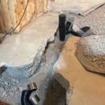 Assembled black fittings with clamps in the foreground and upright drain stack along the trench in Draper.