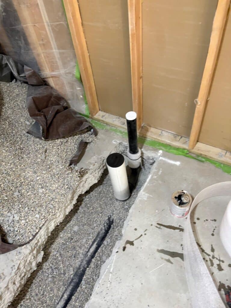 New vertical drain stubs set in cut slab for laundry and kitchen rough-in work in a Draper basement remodel.