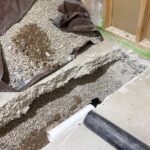 White and black drain pipe lengths staged beside a gravel-filled slab cut for rough-in in Draper basement.