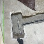 Opened concrete trench showing black sewer pipe and fittings bedded in gravel for underground work in Draper.