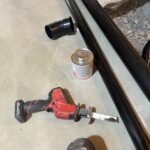 Reciprocating saw, solvent cement, elbow, and long black pipe lengths staged on slab from the stocked van in Draper.