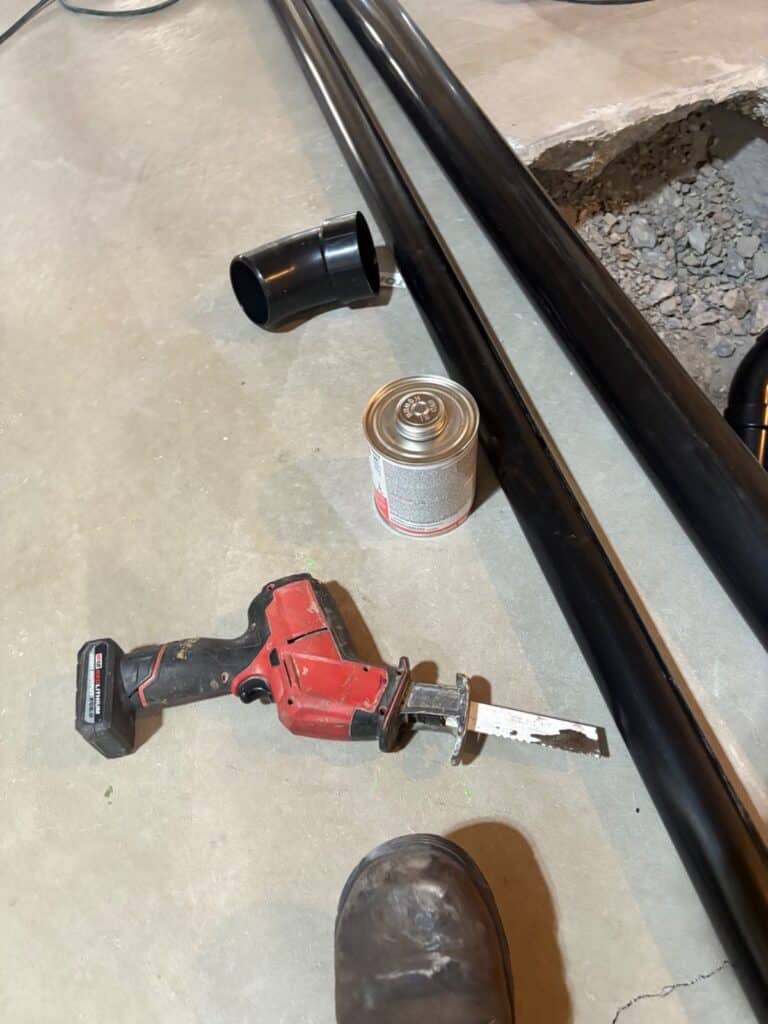 Reciprocating saw, solvent cement, elbow, and long black pipe lengths staged on slab from the stocked van in Draper.