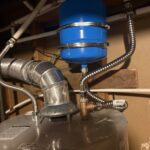 Blue expansion tank strapped above Bradford White water heater with flexible water lines and vent collar in Bountiful UT