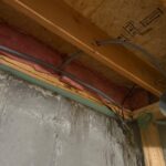 Gray supply tubing at rim joist with brass fittings near foundation wall after ice maker valve work Sandy