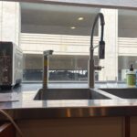 Installed kitchen faucet pair on stainless double sink with city view through large window