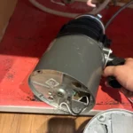Removed gray disposal motor housing held open showing bottom wiring while the old unit is taken out in Midvale.