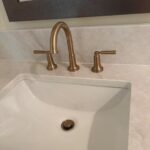 Close view of brass widespread faucet spout and handles over white sink after Midway installation