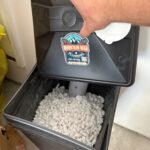Open brine tank filled with softener salt pellets in garage with Mountain Man Plumbing sticker Midway