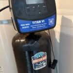 Holts Titan VI Pro-Max control head on black mineral tank with Mountain Man Plumbing sticker in Midway utility space