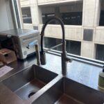 Modern pull-down kitchen faucet and separate spout on double stainless sink overlooking city buildings