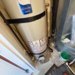 Base of new Bradford White water heater on concrete floor beside drain area in Salt Lake City condo mechanical room.