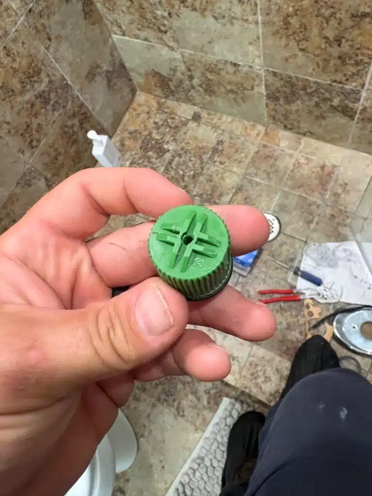 Hand holding broken green plastic temperature plunger from a Grohe shower valve in Sandy, Utah