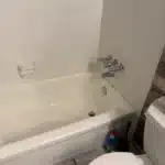 Full view of alcove tub with three-handle chrome valve beside toilet before drain and valve repair Salt Lake City