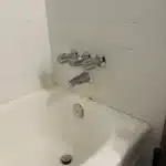 Rebuilt three-handle chrome shower valve and spout on tiled wall above tub in Salt Lake City