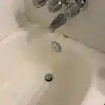 Three-handle chrome tub shower valve and spout over stained tub drain area before rebuild in Salt Lake City bathroom