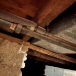 Older threaded pipe coupling and line near floor framing where a valve leak was diagnosed