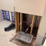 Wide open basement wall with PEX runs, black drain, gray tub catch, and new stops after Sandy leak repair
