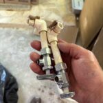 Hand holding two removed chrome stops with broken cream CPVC elbows from Sandy UT remodel flood job