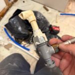 Hand holding removed gray fixture shutoff with cream CPVC elbow after snap failure during Sandy UT remodel leak repair