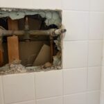 Closer view of opened tile revealing three-handle shower valve stems and copper stubs before Moen install in Sandy