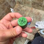 Hand holding broken green plastic temperature plunger from Grohe shower valve after high pressure in Sandy UT