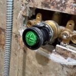 Black cartridge housing with green control pulled forward from brass Grohe shower valve during Sandy Utah inspection