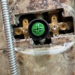 Green plastic temperature control piece seated in black housing on brass Grohe shower valve body during Sandy UT service