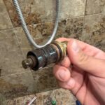Hand holding removed Grohe thermostatic cartridge with stem and seals from Sandy Utah shower valve
