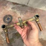 Removed brass three-handle shower valve body held outside after shower valve replacement work in Sandy Utah bathroom
