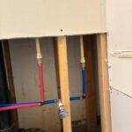Red and blue PEX with brass adapters and chrome stop installed through open stud bay in Sandy UT remodel