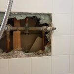 Tiled shower wall opening exposing old three-handle valve and copper lines during Sandy Utah shower valve replacement