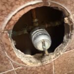 Round tile access opening showing shutoff valve and copper lines under a Millcreek Utah bathroom floor.